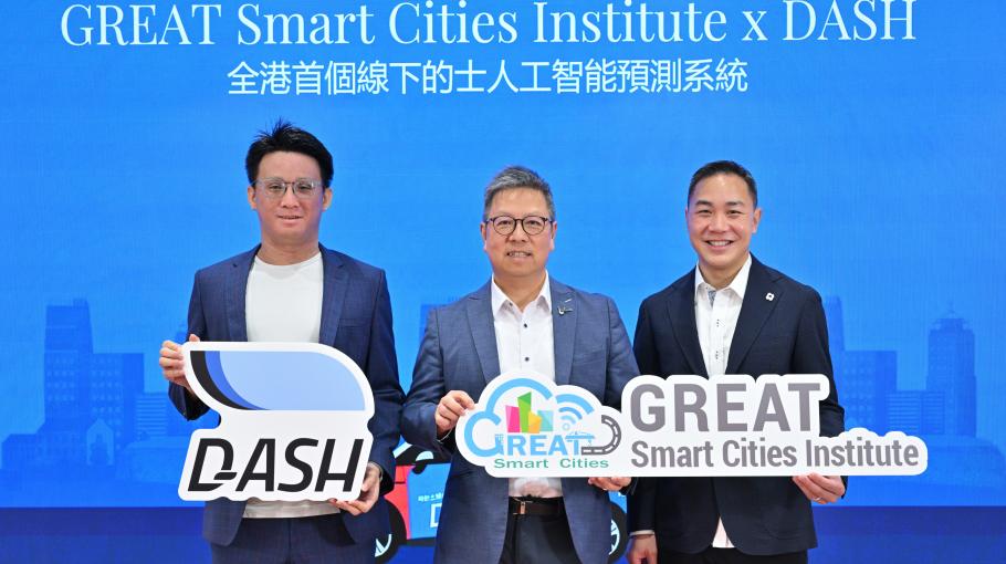 A group photo of Jason Ma, the co-founder of DASH, Prof. Hong K. Lo, Director of GSCI and Mr Michael Chan, co-founder of DASH holding event signs at a press conference. The background is a large blue LED screen featuring a faint city skyline graphic, with white text that reads "GREAT Smart Cities Institute x DASH" and a line of traditional Chinese text below it. The man on the left wears a blue patterned blazer over a white shirt and holds a white "DASH" sign. Professor Hong K. Lo